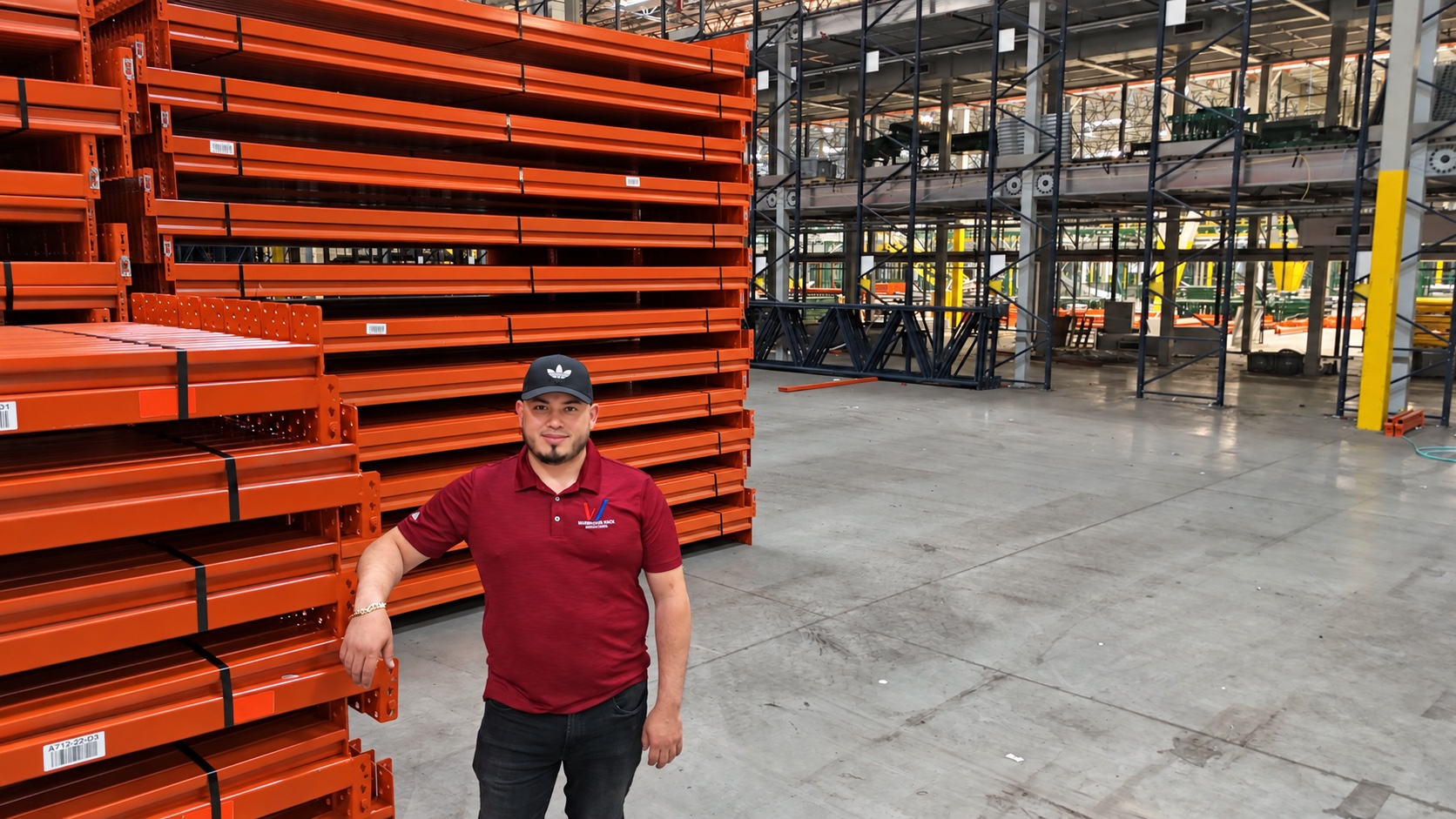 Luis of Warehouse Rack Installation beside staged pallet-rack components in a large distribution facility